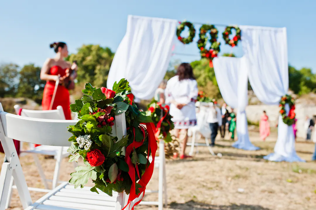Outdoor wedding ceremony with a white draped arch, floral wreaths and a violinist