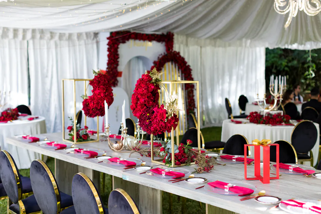 Banquet table under a white tent with red rose arrangements in gold frames
